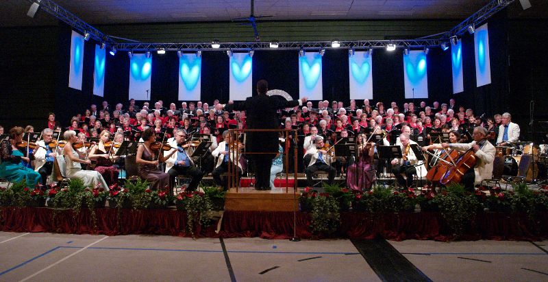 Die Sängerinnen und Sänger des Projektchores stehen auf der festlich geschmückten Bühne der Stadthalle Linden zusammen mit dem Johann-Strauss-Orchester